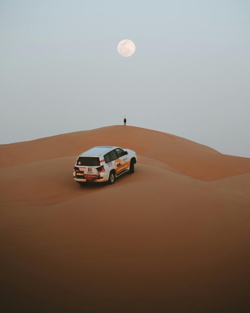 Capture the serene beauty of a desert night under a full moon in Abu Dhabi, featuring endless dunes and a lone car.